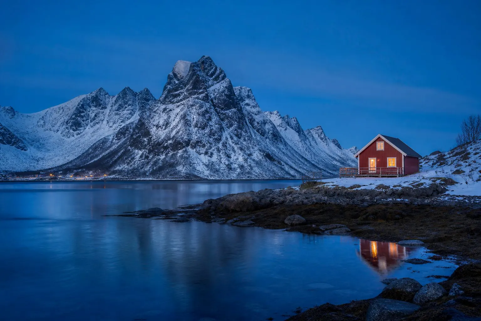 Cabane rouge au bord d’un fjord enneigé à l’heure bleue