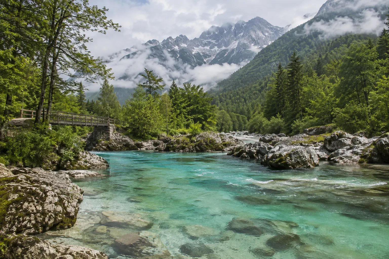 Rivière turquoise de la Soča, passerelle en bois et sommets calcaires après la pluie